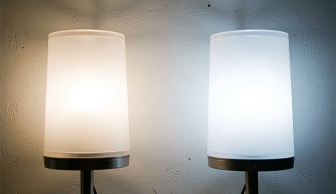 Twee identieke schemerlampen naast elkaar tegen een lichte wand, links met duidelijk geler licht en rechts met koeler, witter licht.